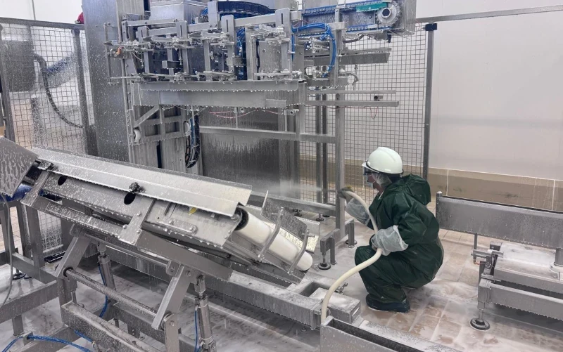 Worker in protective clothing using a hose to clean automated machinery and conveyor systems during sanitation in a food processing facility.