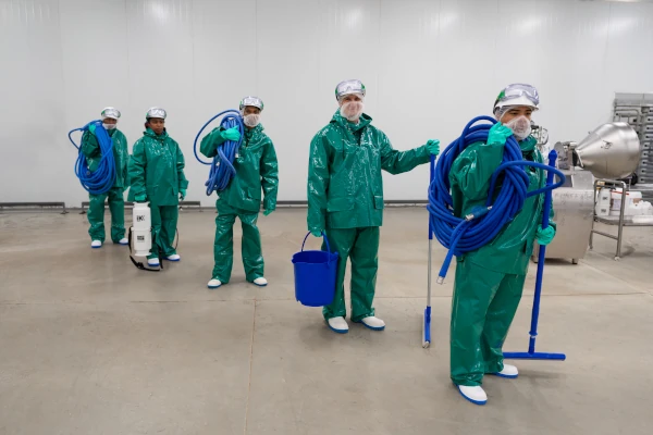 Food processing sanitation team wearing full protective equipment and carrying cleaning tools inside a production facility, demonstrating hygienic cleaning, food safety, and sanitation readiness.
