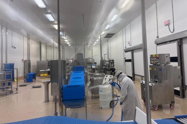 Food processing facility with a worker in protective clothing cleaning stainless steel equipment and conveyor systems.