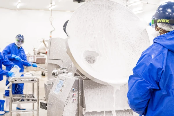 Food production workers in protective clothing cleaning large industrial processing equipment with foam, supporting food safety and sanitation standards.